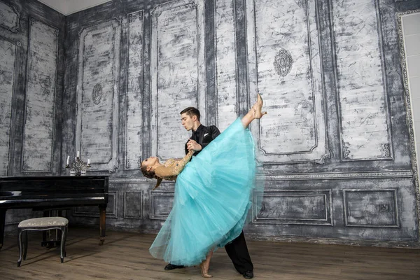 a young man in a black suit is dancing with a girl in a turquoise dress in the dance hall