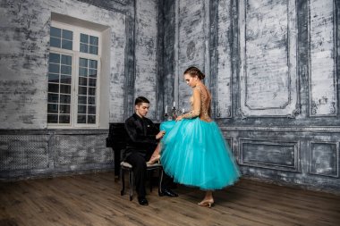 Genç bir adam piyanonun başında oturur ve yanındaki dans partnerine bakar.