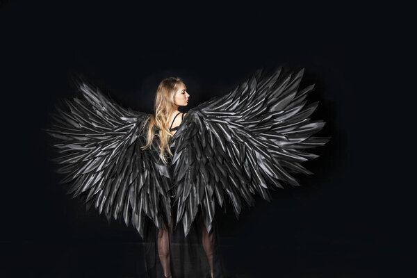 Beautiful blonde girl in a black suit with black wings on a black background