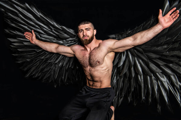 Handsome athletic man in black angel costume on black background