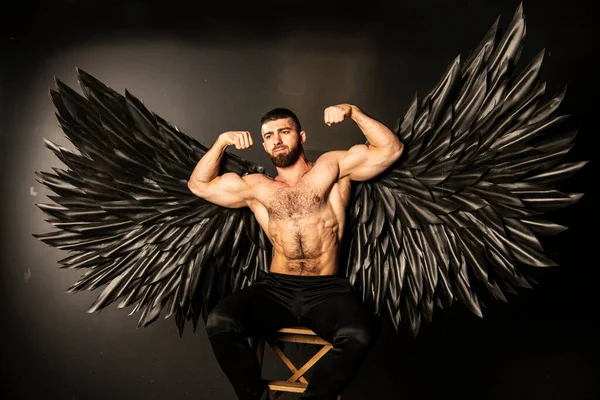 handsome athletic man in black angel costume on black background