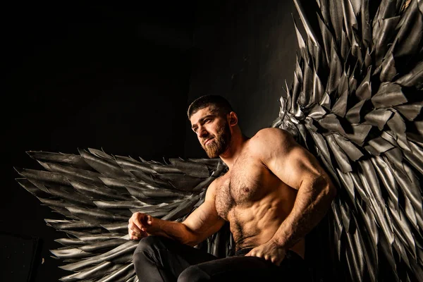 handsome athletic man in black angel costume on black background