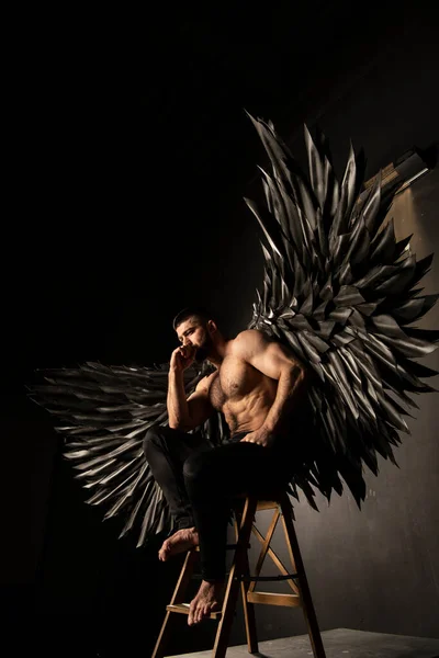 handsome athletic man in black angel costume on black background