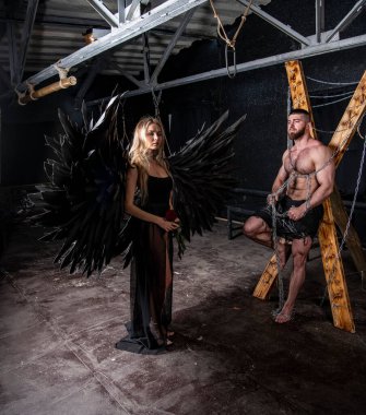 Siyah kanatlı güzel bir kız ve siyah arka planda zorluklarla boğuşan yakışıklı kaslı bir adam.