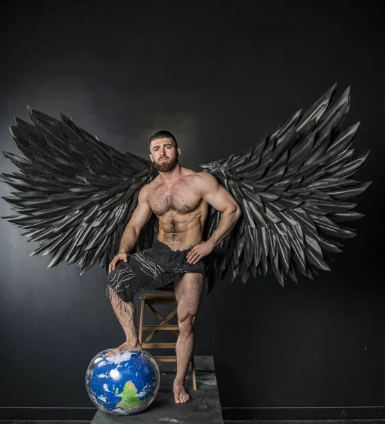 handsome muscular man in angel costume with black wings on black background