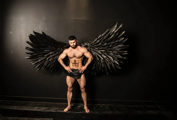 handsome muscular man in angel costume with black wings on black background