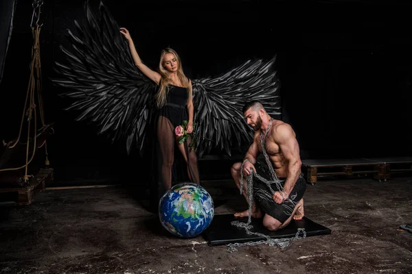 黒羽の天使の衣装を着た美しい女の子と黒の背景で苦労してハンサムな筋肉質の男 — ストック写真