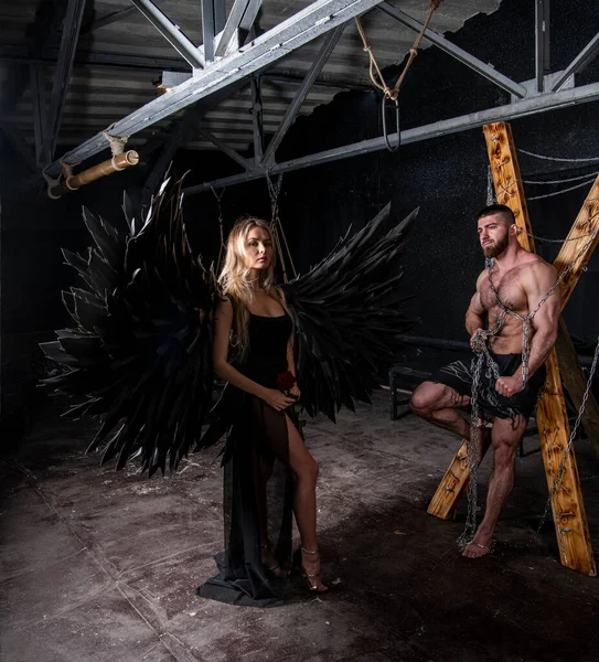 黒羽の天使の衣装を着た美しい女の子と黒の背景で苦労してハンサムな筋肉質の男 — ストック写真