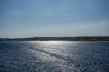 Mavi deniz, berrak gökyüzü ve çöl kıyı şeridi olan manzara.