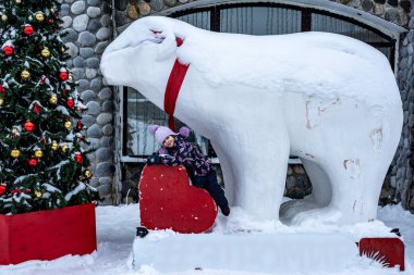 Mor şapkalı güzel bir kız oyun parkının arka planında karda oynuyor.