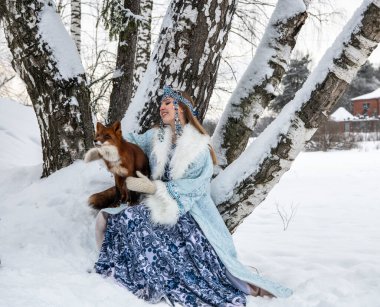 Rus güzeli ulusal bir kostüm içinde ve kışın karlı bir ormanda kızıl tilki 