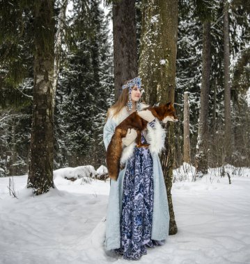 Rus güzeli ulusal bir kostüm içinde ve kışın karlı bir ormanda kızıl tilki 