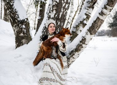 Rus güzeli ulusal bir kostüm içinde ve kışın karlı bir ormanda kızıl tilki 