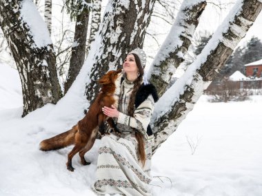 Rus güzeli ulusal bir kostüm içinde ve kışın karlı bir ormanda kızıl tilki 