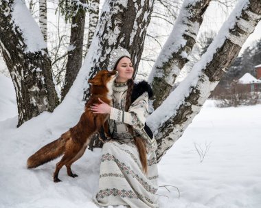 Rus güzeli ulusal bir kostüm içinde ve kışın karlı bir ormanda kızıl tilki 