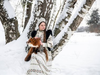Rus güzeli ulusal bir kostüm içinde ve kışın karlı bir ormanda kızıl tilki 