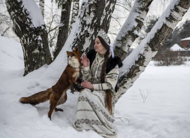 Rus güzeli ulusal bir kostüm içinde ve kışın karlı bir ormanda kızıl tilki 