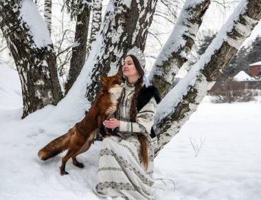 Rus güzeli ulusal bir kostüm içinde ve kışın karlı bir ormanda kızıl tilki 
