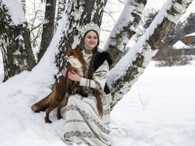 Rus güzeli ulusal bir kostüm içinde ve kışın karlı bir ormanda kızıl tilki 