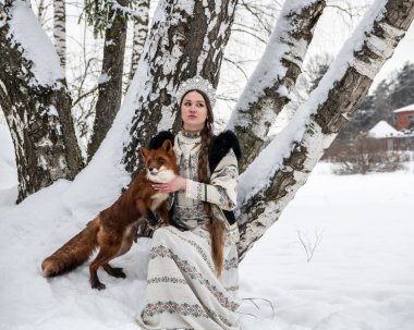 Rus güzeli ulusal bir kostüm içinde ve kışın karlı bir ormanda kızıl tilki 