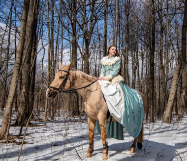 Mavi elbiseli güzel bir kız ve bahar ormanında açık kahverengi bir at.