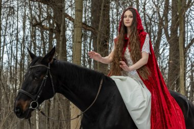 Beyaz elbiseli güzel bir kız ve bahar ormanında siyah atlı kırmızı bir pelerin.