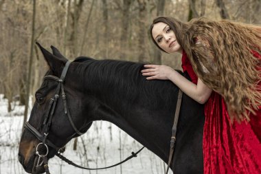 Beyaz elbiseli güzel bir kız ve bahar ormanında siyah atlı kırmızı bir pelerin.