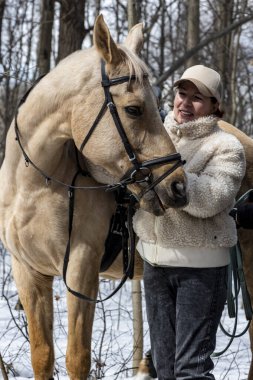 Bahar ormanında açık kahverengi atlı, bej şapkalı ve kürklü bir kadın.