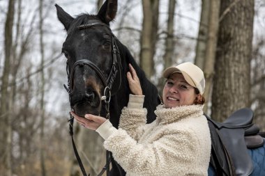 Bahar ormanında bej şapkalı, kürklü siyah atlı bir kadın.