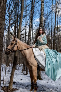 Mavi elbiseli güzel bir kız ve bahar ormanında açık kahverengi bir at.