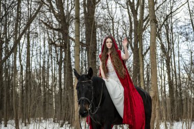 Beyaz elbiseli güzel bir kız ve bahar ormanında siyah atlı kırmızı bir pelerin.