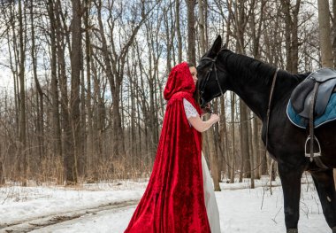 Beyaz elbiseli güzel bir kız ve bahar ormanında siyah atlı kırmızı bir pelerin. 
