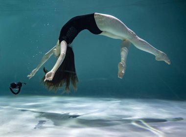 Siyah mayo giymiş, mavi arka planda siyah bir telefon ahizesiyle su altında poz veren güzel bir kız.