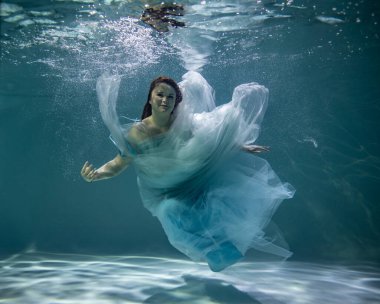   Suyun altında poz veren kırmızı saçlı, mavi elbiseli güzel bir kadın. 