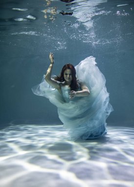  Suyun altında poz veren kırmızı saçlı, mavi elbiseli güzel bir kadın. 