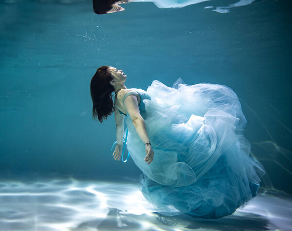   beautiful woman with red hair in a lush blue dress posing underwater 