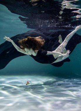 Siyah mayo giymiş güzel bir kız ve siyah pareo su altında mavi bir arka planda akvaryumda balıklarla oynuyor.
