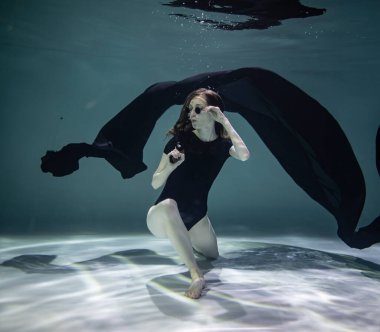 Siyah pareolu siyah mayo giymiş güzel bir kız mavi arka planda, su altında elinde siyah bir tabanca tutuyor.