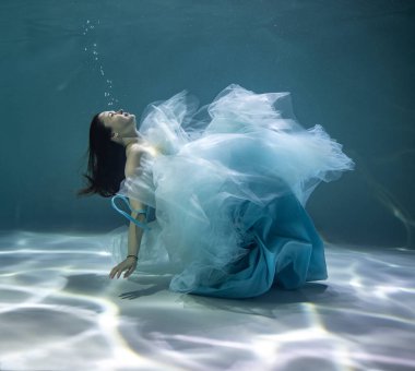 Su altında mavi bir arka planda beyaz ve mavi balo elbisesi içinde güzel bir kız. 