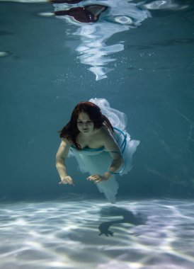 Su altında mavi bir arka planda beyaz ve mavi balo elbisesi içinde güzel bir kız. 