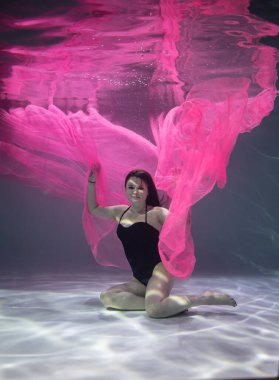 Suyun altında mavi arka planda kırmızı pareolu siyah mayo giyen güzel bir kız. 