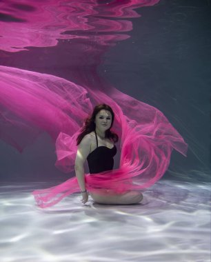 Suyun altında mavi arka planda kırmızı pareolu siyah mayo giyen güzel bir kız. 