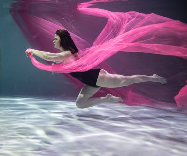 Suyun altında mavi arka planda kırmızı pareolu siyah mayo giyen güzel bir kız. 