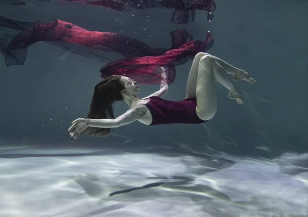 青い背景に水中に赤いパレオのある赤い水着の美しい女の子 — ストック写真