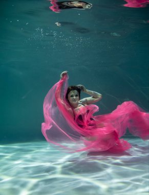 Siyah mayo giymiş güzel bir kız ve mavi arka planda pembe bir pareo ile su altında.