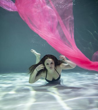 Siyah mayo giymiş güzel bir kız ve mavi arka planda pembe bir pareo ile su altında.