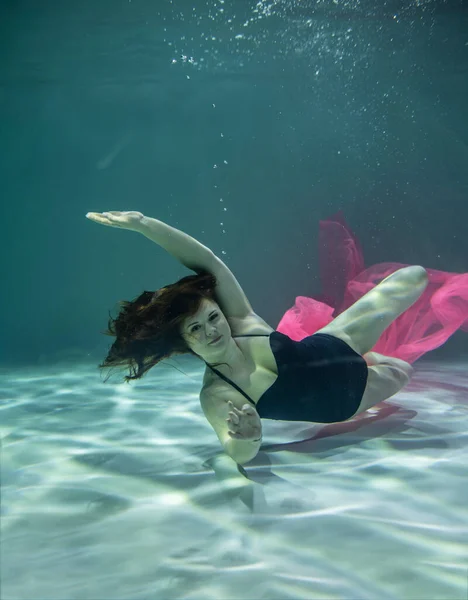 黒の水着の美少女と青い背景にピンクのパレオを水中で — ストック写真