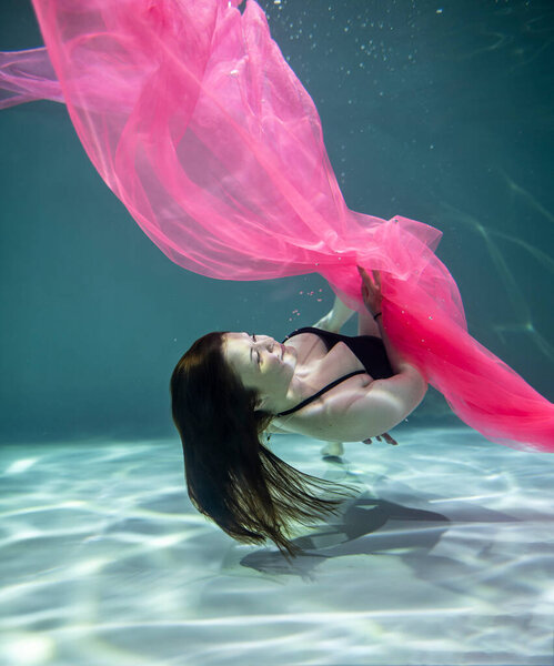 красивая девушка в черном купальнике и с розовым парео под водой на синем фоне