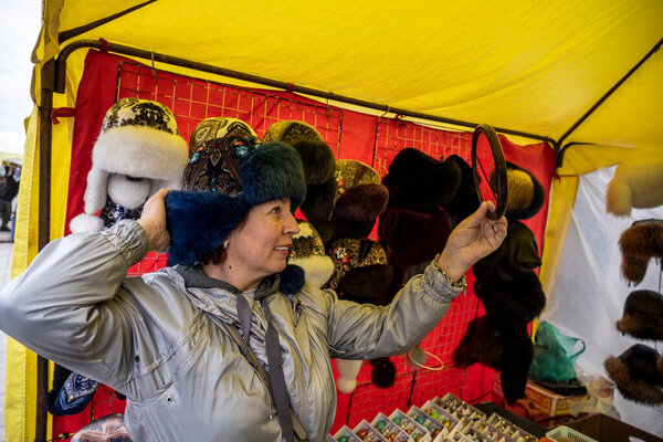 Женщина в сером плаще купила синюю национальную шляпу на уличной ярмарке