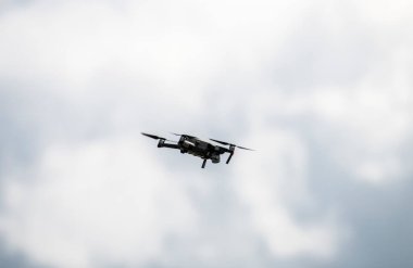 Yerin üstünde süzülen bir dron, mavi ve beyaz bir gökyüzünün arka planına karşı uçar.
